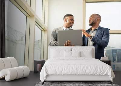 two young black business men standing together holding a laptop, discussing business Wall mural