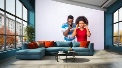 young african man making a phone call too close to a lady who is blocking her ears with her fingers Wall mural