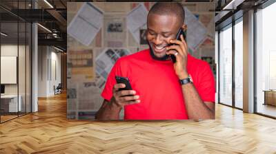 young black man making a phone call and holding another phone, smiling Wall mural