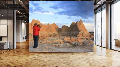 Man in red jacket and cowboy hat taking photographs in Badlands National Park at sunrise Wall mural