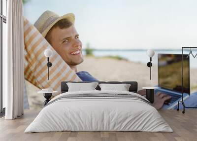 Attractive young man relaxing at the beach with laptop Wall mural