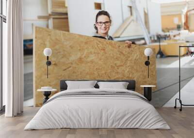 Friendly female woodworker holding a sheet of chipboard Wall mural