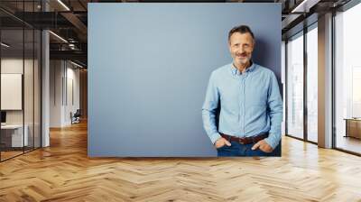 smiling bestager stands in front of a blue wall and looks into the camera Wall mural