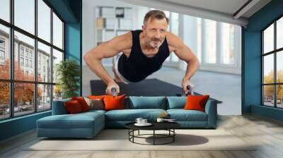 Sportive middle-aged man doing push-ups on handles Wall mural