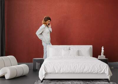 Woman stands talking on phone in front of red wall and looks down, copy space Wall mural