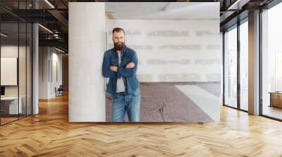 Young bearded man standing with folded arms Wall mural