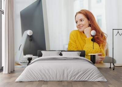 Young cheerful woman sitting in front of computer Wall mural