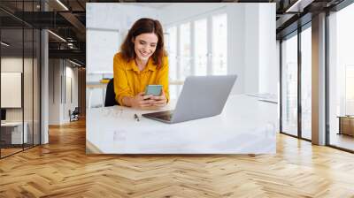 young modern business woman sitting at desk and looking at her cell phone in office Wall mural