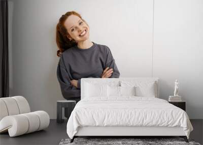 young redhead woman stands laughing with folded arms in front of white wall Wall mural