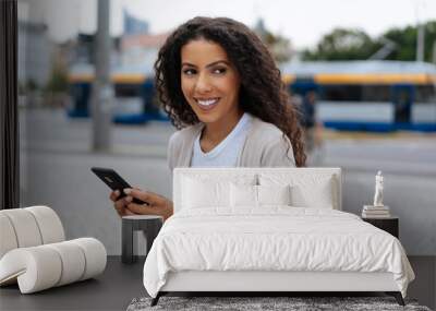 Young woman holding her mobile in an urban street Wall mural