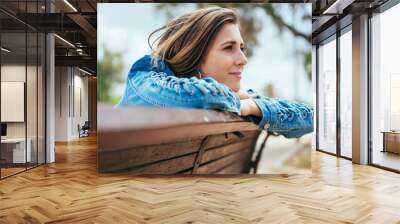 Young woman sitting on a bench daydreaming Wall mural