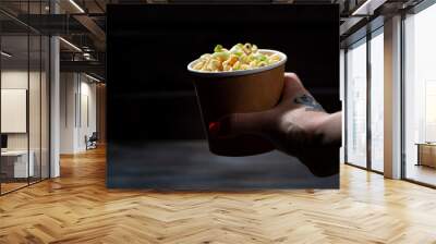 paper cup with chinese egg noodles in the hand of a person on dark background Wall mural