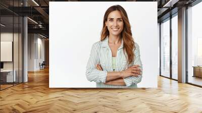 Ambitious and confident business woman, female entrepreneur standing with arms crossed and smiling self-assured at camera, saleswoman against white background Wall mural