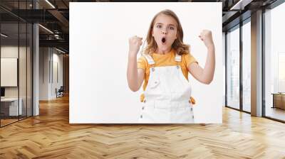 Amused cheerful young blond girl child, celebrating victory, feeling excited like winner, fist pump triumphing, say yes hooray, pouting proudly, stand white background enthusiastic Wall mural