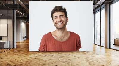 Attractive unshaven young dark-skinned male in red tshirt widely smiling laughing at funny picture on internet. Positive facial expressions and emotions Wall mural