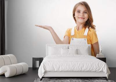 Cheerful proud cute little girl showing achievement, introduce cool copy space, raise hand hold something on blank space, smiling happily, posing near white background in summer outfit Wall mural