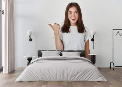 Cheerful young woman pointing thumb left at copy space, showing promo banner on white background Wall mural