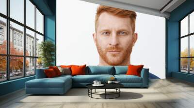 Close-up shot of serious-looking handsome adult european man with red hair and beard staring at camera with focused and determined expression, standing in strict pose over gray background Wall mural