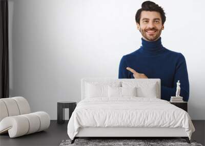 Confident, good-looking happy smiling caucasian man with bristle in stylish high neck sweater, proudly pointing left and look camera, recommend promo, advertise product, white background Wall mural