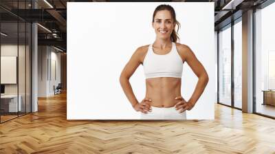 Confident sportswoman in white sportsbra, holding hands on waist, fitness trainer standing in power pose, workout in gym, white background Wall mural