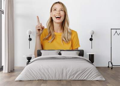 Excited smiling blond girl looking and pointing up with amused face, reading promo text, banner on top, standing in yellow tshirt over white background Wall mural