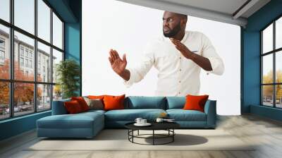 Funny and playful adult African American guy with beard, standing in profile in martial arts pose with raised palms, frowning and staring left with angry and evil expression to fight with enemy Wall mural