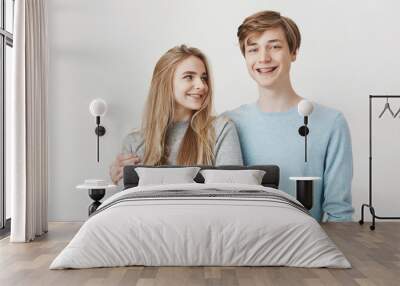 Girlfriend knows boyfriend prepared something for anniversary. Portrait of two friendly caring siblings, hugging and smiling broadly, wearing shiny braces. Girl looking at guy who dare to cuddle her Wall mural