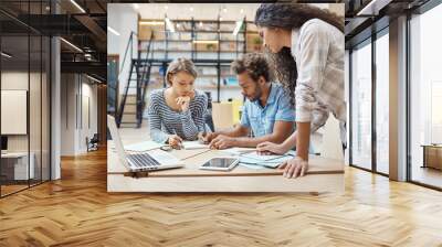 Group of three young multi-ethnic successful business people sitting in coworking space, talking about new project of competitor team, making plans to bypass their project. Wall mural