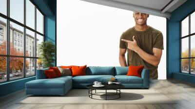 Guy presenting new copy space to us with cheerful friendly smile holding hand in pocket pointing left, grinning having good positive mood standing casually over gray background Wall mural