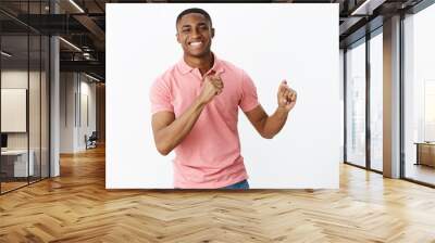 Handsome charming young african american masculine guy in pink polo shirt gesturing with hands as dancing, having fun smiling joyfully spending great time at friends party over white wall Wall mural