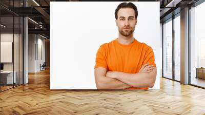 Handsome european man cross arms on chest, looking confident and self-assured, standing in orange tshirt over white background Wall mural