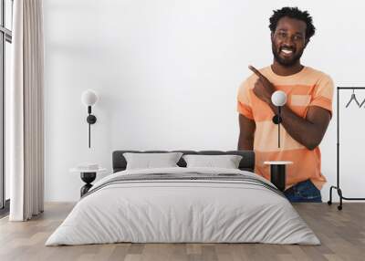 Handsome young african-american guy with bristle in striped t-shirt and jeans pointing upper left corner, smiling, promote or recommend some link or product, standing white background cheerful Wall mural