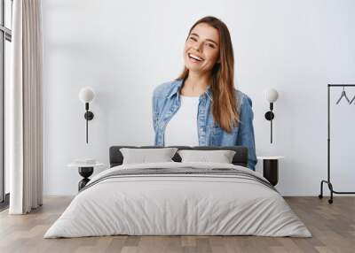 Happy carefree woman with joyful expression, smiling while standing in relaxed pose against white background, holding hands in jeans pockets Wall mural