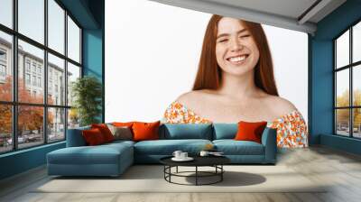 Happy redhead girl close her eyes and laughing, smiling carefree, imaging smth funny, standing over white background Wall mural