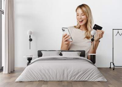 Happy smiling woman with mobile phone, showing credit card and laughing, demonstrating paying app, bank offer for contactless online shopping pay, white background Wall mural