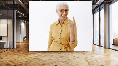 Her sould is young. Portrait of joyful pleased and carefree enthusiastic grandmother with grey hair in stylish sunglasses and yellow coat sticking out tongue showing rock n roll gesture Wall mural