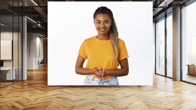 Image of smiling Black woman holding hands together and looking at camera helpful, assisting customer or client, standing friendly against white background Wall mural