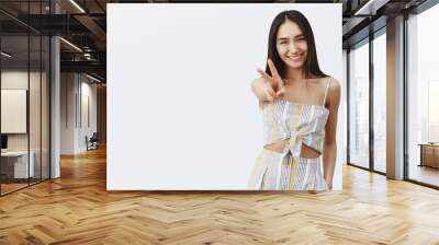 Let us travel world and enjoy life. Portrait of good-looking feminine and elegant dark-haired female with mole under lip smiling broady, pulling hand towards camera in peace or victory gesture Wall mural