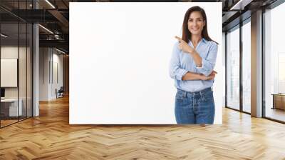 Motivated good-looking adult female employee curiously pointing left, introduce sideways copyspace, smiling joyful, discuss project with coworkers, stand blue-collar shirt white background Wall mural