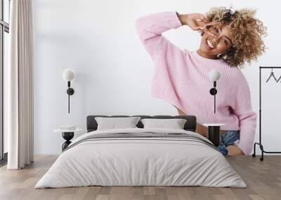 Oh yeah, girl enjoys winter holidays. Charismatic carefree and silly cute african american woman with blond afro haircut waving and tilting head showing peace sign on eye and smiling happily Wall mural