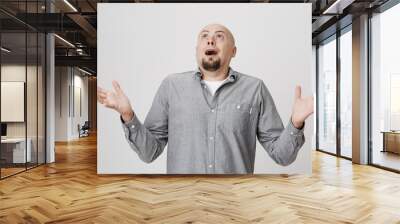 Portrait of an adult man looking up in the sky with surprised or shocked expression over white background. Person spreads his hands not having clue of what is happening. Wall mural