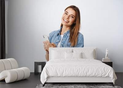 Portrait of beautiful millennial girl with white smile, messaging, using chat app on smartphone and looking at camera, standing over white background Wall mural