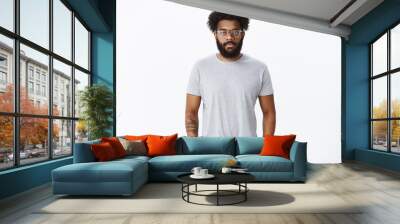 Portrait of calm and relaxed unemotional african american mature man with beard in glasses with pierced nose and tattoos holding hands in pockets looking at camera indifferent and unbothered Wall mural