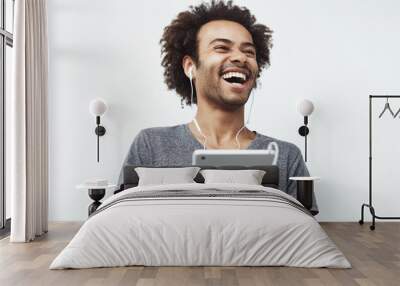 Portrait of cheerful happy african man in headphones laughing holding tablet talking or watching and enjoying a comedy show or browsing over white background. Wall mural