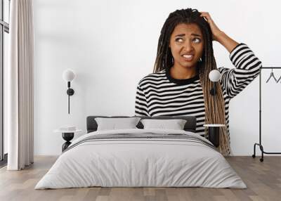 Portrait of confused black girl looking awkward and unsure, scratching head and looking aside with indecisive face expression, white background Wall mural