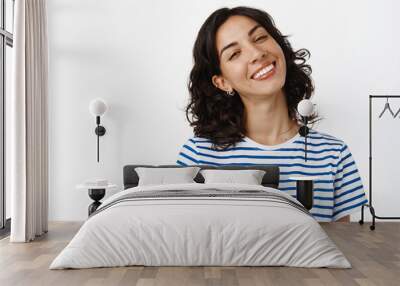 Portrait of happy pretty girl with dark curly hair, pierced nose, smiling white teeth, looking positive and upbeat, enjoying life, standing in summer t-shirt against white background Wall mural