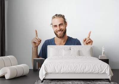 Portrait of joyful beautiful men with fashionable hairstyle and beard in blue t shirt laughing and pointing upside with two hands. Copy space for advertisement. Wall mural