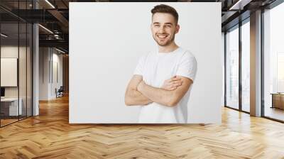 Portrait of pleased confident and accomplished european guy with stylish haircut standing unshaven over gray background crossing hands on chest smiling joyfully and satisfied at camera Wall mural