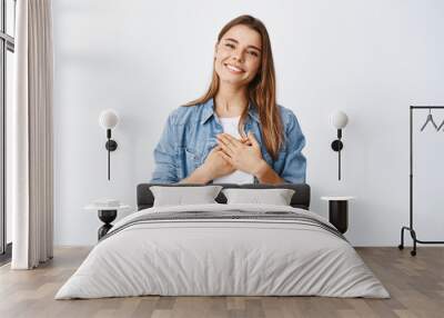 Portrait of touched young woman feeling flattered, holding hands on heart and smiling white teeth, say thank you, appreciate help, being grateful for nice gesture, white background Wall mural