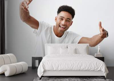 Portrait of young attractive dark-skinned man with afro hairstyle in white casual t-shirt smiling with teeth, gesticulating with hands in camera, looking in camera with happy and excited expression Wall mural